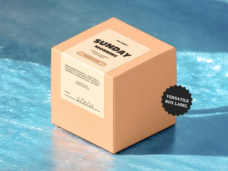 May include: A brown cardboard box with a white label that says "SUNDAY MORNING" in black text. The label also says "NATURAL COCONUT SOY WAX CANDLES" and "GRAPEFRUIT & MINT". The box is sitting on a blue surface.